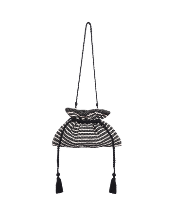 The Cinched Bag by THE GREAT. SU23 is a black and cream striped cotton handbag with a woven tassel, drawstring closure, and braided shoulder strap for a bohemian touch.