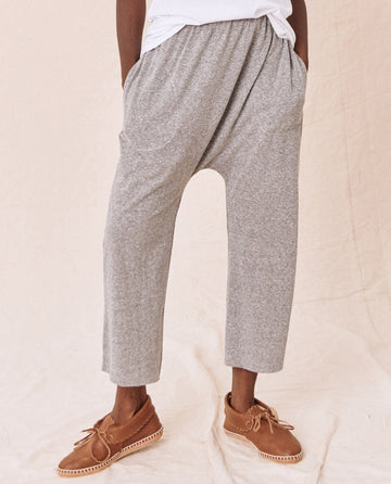 A person sporting The Jersey Crop in Heather Grey, designed by THE GREAT. CORE KNITS, along with brown moccasins, stands against a beige background.