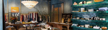 A boutique interior with clothing racks, a central table displaying items, shelves with products, and a large decorative ceiling light.