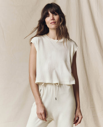 A person with long hair wears THE GREAT.'s handcrafted The Square Tee in Washed White, standing in front of a light-colored fabric backdrop.