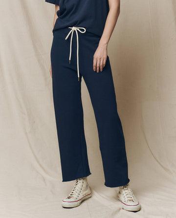 A person wearing The Wide Leg Cropped Sweatpant in True Navy, by THE GREAT. FALL 23 KNITS, features a drawstring waist and wide cropped legs, perfectly paired with white high-top sneakers. These 100% cotton pants offer stylish comfort and easy elegance.