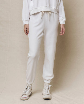 A person in THE GREAT. HOL 24 KNITS' The Stadium Sweatpant in True White, paired with a white sweatshirt and sneakers, captures the essence of vintage athletic wear against a neutral background.