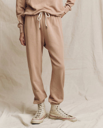 A person is elegantly standing on a light fabric backdrop, wearing The Stadium Sweatpant in Biscotti from THE GREAT. HOL 24 KNITS, paired with a matching top and white high-top sneakers.