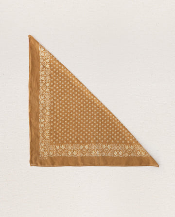 Introducing The Bandana -- Small -- Marigold by THE GREAT. SP24 D2, a vintage-inspired handkerchief crafted from 100% cotton. This exquisite piece showcases a brown triangular design adorned with an intricate floral and geometric border pattern set against a crisp white background.