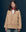 Amidst a dark backdrop, a person exudes outdoor fashion elegance in THE GREAT. SP25 COLLECTORS' The Barn Jacket - Golden, featuring a distinguished brown collar and accessorized with a chic red scarf.