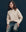 A person with long hair wearing The Classic Cable Pullover in cream from THE GREAT. SP25 COLLECTORS and jeans sits against a dark background.