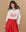 A woman with wavy brown hair models THE GREAT. SP25 MOM GRAPHICS "The College Sweatshirt" in washed white, featuring "The Greatest Mom" in a red heart, paired with a high-waisted red skirt—perfect Mother’s Day sweatshirt inspo.