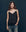 A person with long hair, wearing The Legacy Top by THE GREAT. SP25 COLLECTORS and jeans, stands against a dark background, exuding effortless style with one hand casually tucked in their pocket.