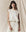 A person with long hair wears THE GREAT.'s handcrafted The Square Tee in Washed White, standing in front of a light-colored fabric backdrop.