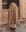 A person stands outside in The Western Field Skirt - Barley by THE GREAT. SP25 D1, paired with a black sweater, maroon shoes, and white socks. Hands are tucked into the skirt's pockets.