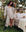 A woman in The Sweatshirt Robe by THE GREAT. PS25 SLEEP stands beside an outdoor bed. Tracy, dressed in a polka dot pajama set and luxurious Light Heather Grey robe, is surrounded by lush green plants and trees, embodying the essence of loungewear staples.