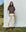 A person stands outdoors against a light backdrop, wearing The Lacrosse Polo in Capital Stripe by THE GREAT. PS25, cream pants, and brown boots.