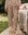 Standing outdoors on a stone path, a person wears THE GREAT. SP25 SLEEP's Easy Sleep Pant in Cream Cowboy—comfortable, cream-colored pajamas with a horse print—paired with light socks. A quilted bed and teddy bear create cozy vibes.