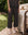 Outdoors, a person stands by a bed wearing THE GREAT. SP25 SLEEP The Easy Sleep Pant in Navy Cowboy and light socks; a teddy bear rests on the bed.