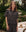 A woman stands outdoors wearing THE GREAT. SP25 SLEEP The Short Sleeve Pajama Shirt in Navy Cowboy; a teddy bear sits on a bench in the background.