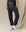 Person wearing The Stadium Sweatpant in washed black from THE GREAT. CORE KNITS with a white drawstring and high-top sneakers, effortlessly blending vintage athletic style against a beige fabric background.