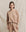 A woman wearing "The College Sweatshirt" in Solid Biscotti by THE GREAT. HOL 24 KNITS stands in front of a beige fabric backdrop, looking at the camera with a neutral expression.